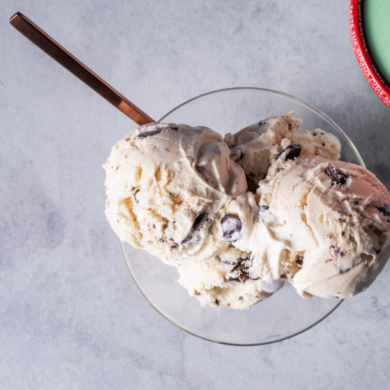 Scoops of creamy organic mint chip ice cream with chocolate pieces in a glass bowl with a spoon.