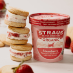 Stack of strawberry ice cream sandwiches next to a Straus Family Creamery organic strawberry ice cream pint with fresh strawberries.